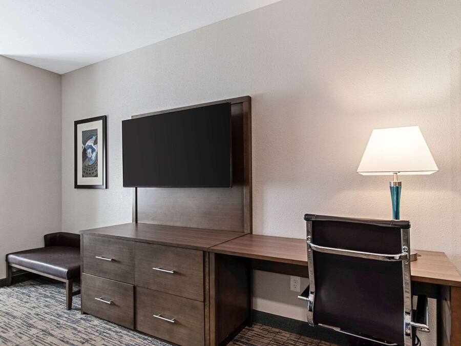 Een hotelkamer met een houten bureau, een flatscreen televisie, een bankje, een lamp en een ingelijst schilderij aan de muur.
