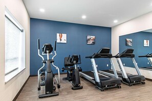 Une salle de sport équipée de machines de cardio, notamment des tapis de course et un appareil elliptique, avec un mur bleu orné d’œuvres d’art.