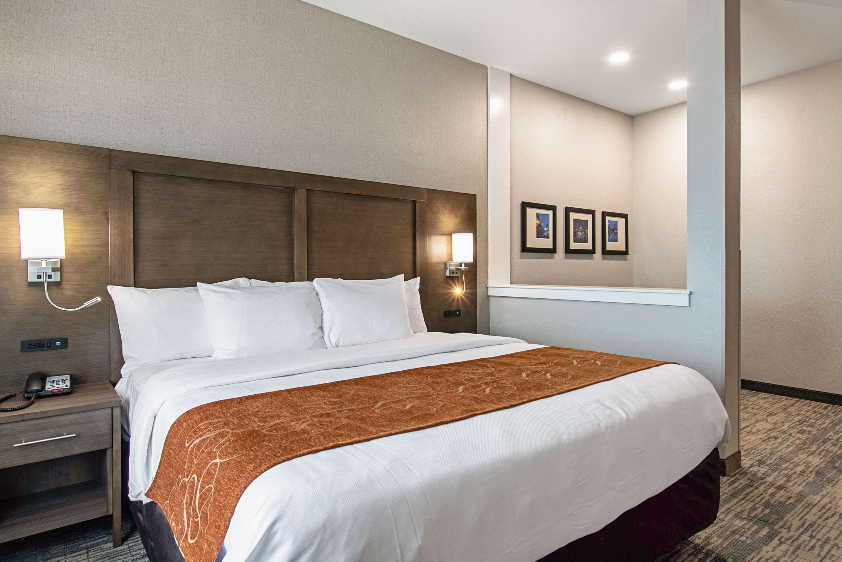 Una habitación de hotel con una cama grande, lámparas de noche, una mesita de noche y un teléfono en la pared.