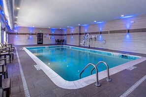 Une piscine intérieure à l’eau claire, entourée de murs carrelés et dotée d’un espace détente avec des chaises.