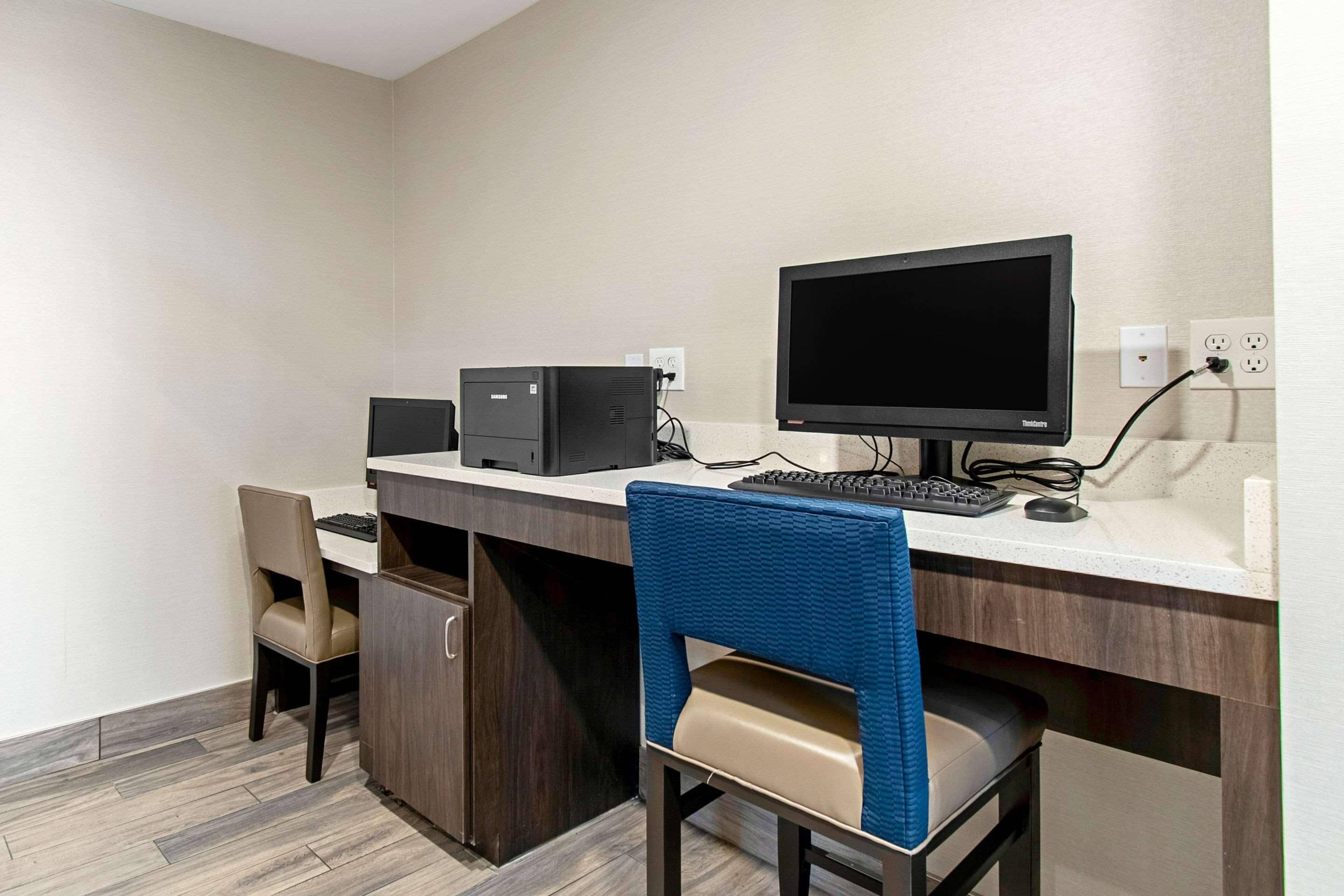 Quarto de hotel com escrivaninha, computador e duas cadeiras.
