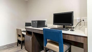 Quarto de hotel com escrivaninha, computador e duas cadeiras.