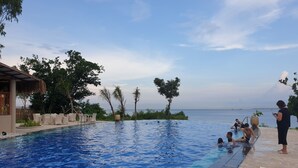 Piscina con vista al mar, rodeada de palmeras y sillones de descanso.