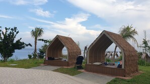 Dos chozas con techo de paja, bancos de madera, un camino empedrado y vista al mar.