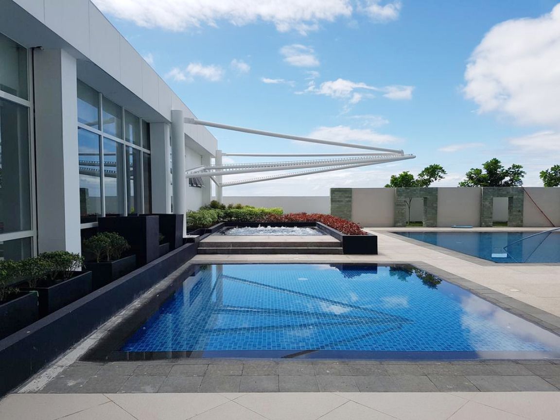 A modern outdoor pool area with a clear blue pool, a white building with large windows, and a pergola structure.