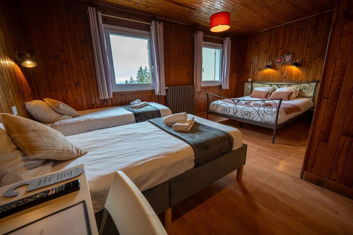 A cozy room with two beds, wooden walls, and a window.