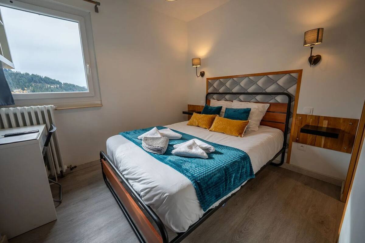 A neatly arranged bedroom with a bed, bedside lamps, and a view of the outdoors.