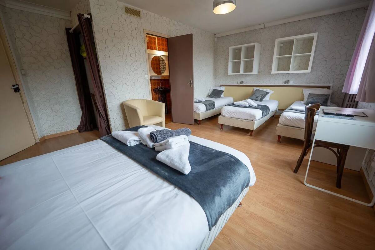 A hotel room with a large bed, two smaller beds, a desk, and a chair.