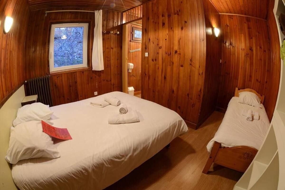 A wooden-paneled room with a large bed, a smaller bed, and a window with a view of trees.
