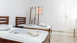 Een nette, minimalistische kamer met twee houten bedden, een klein raam en een witte deur.