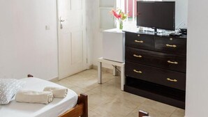 Een slaapkamer met een houten plafond, een bed, een dressoir, een televisie en een raam met bloemen.