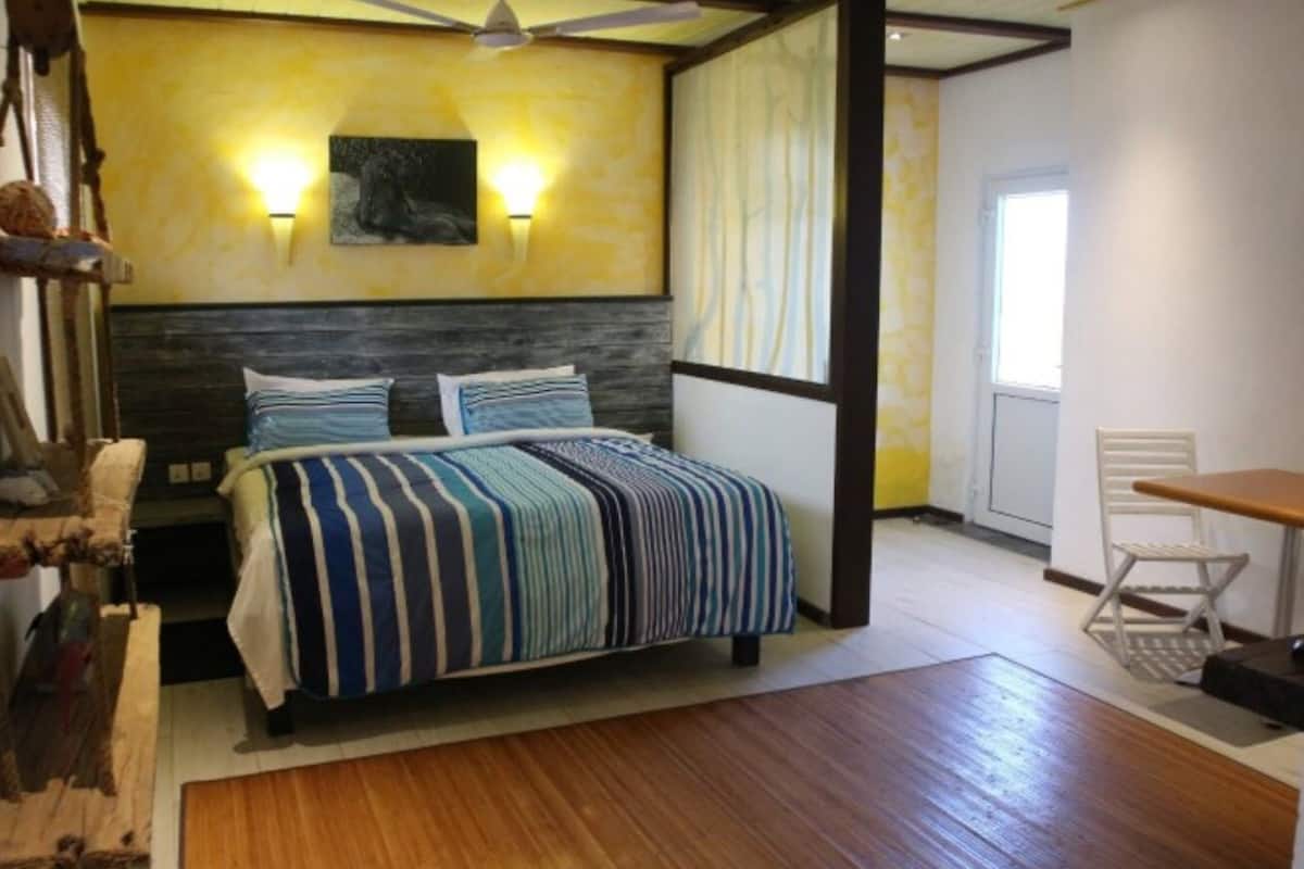 Quarto com cama, escrivaninha, cadeira, ventilador de teto e janela.