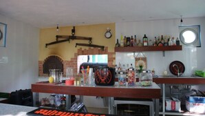 A bar area with a brick oven, shelves with bottles, and various bar tools. - Tom's Garden (Senya Beraku)