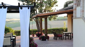 Um pátio externo com piso de tijolos, móveis de madeira e plantas em vasos.