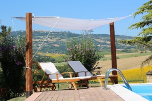Zona de piscina con dos sillones de descanso y una sombrilla, con vistas a un paisaje pintoresco con colinas y un castillo a la distancia.