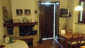 Uma sala de estar acolhedora com lareira, uma mesa de jantar e uma TV fixada na parede.
