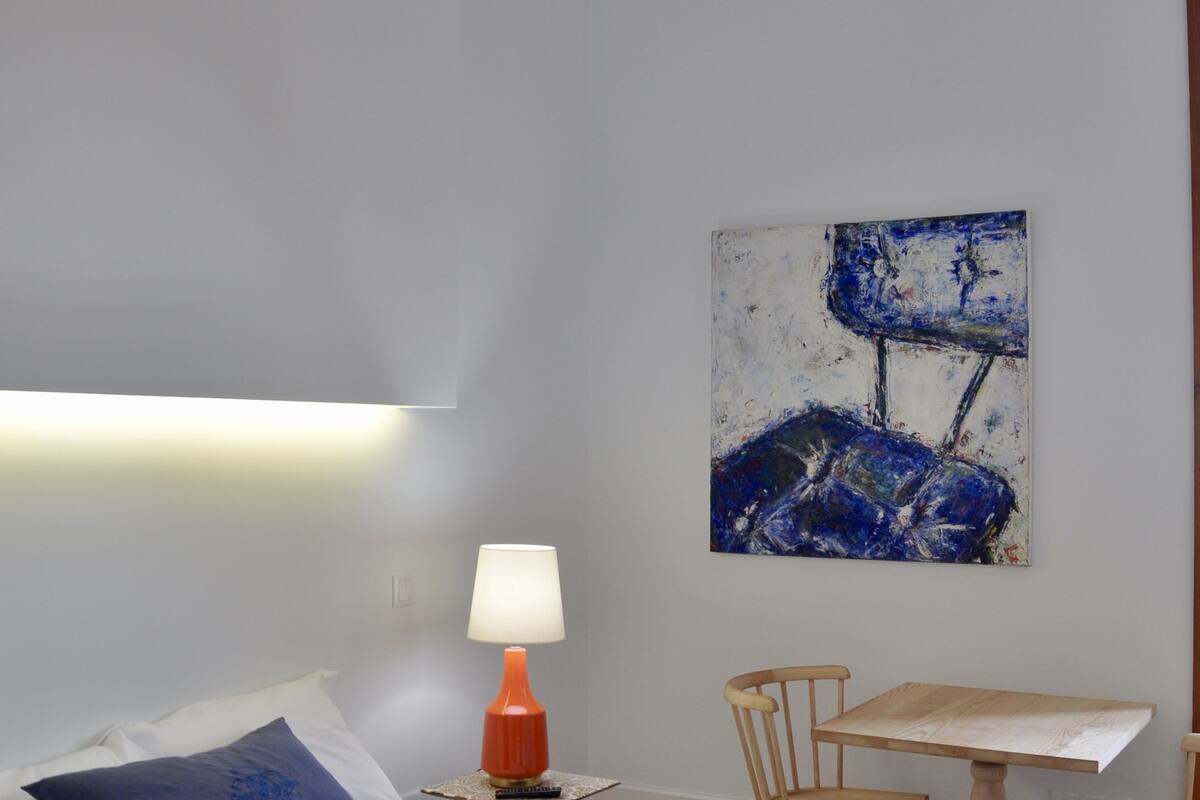 A bedroom with a bed, a desk, a chair, a lamp, and a painting on the wall.