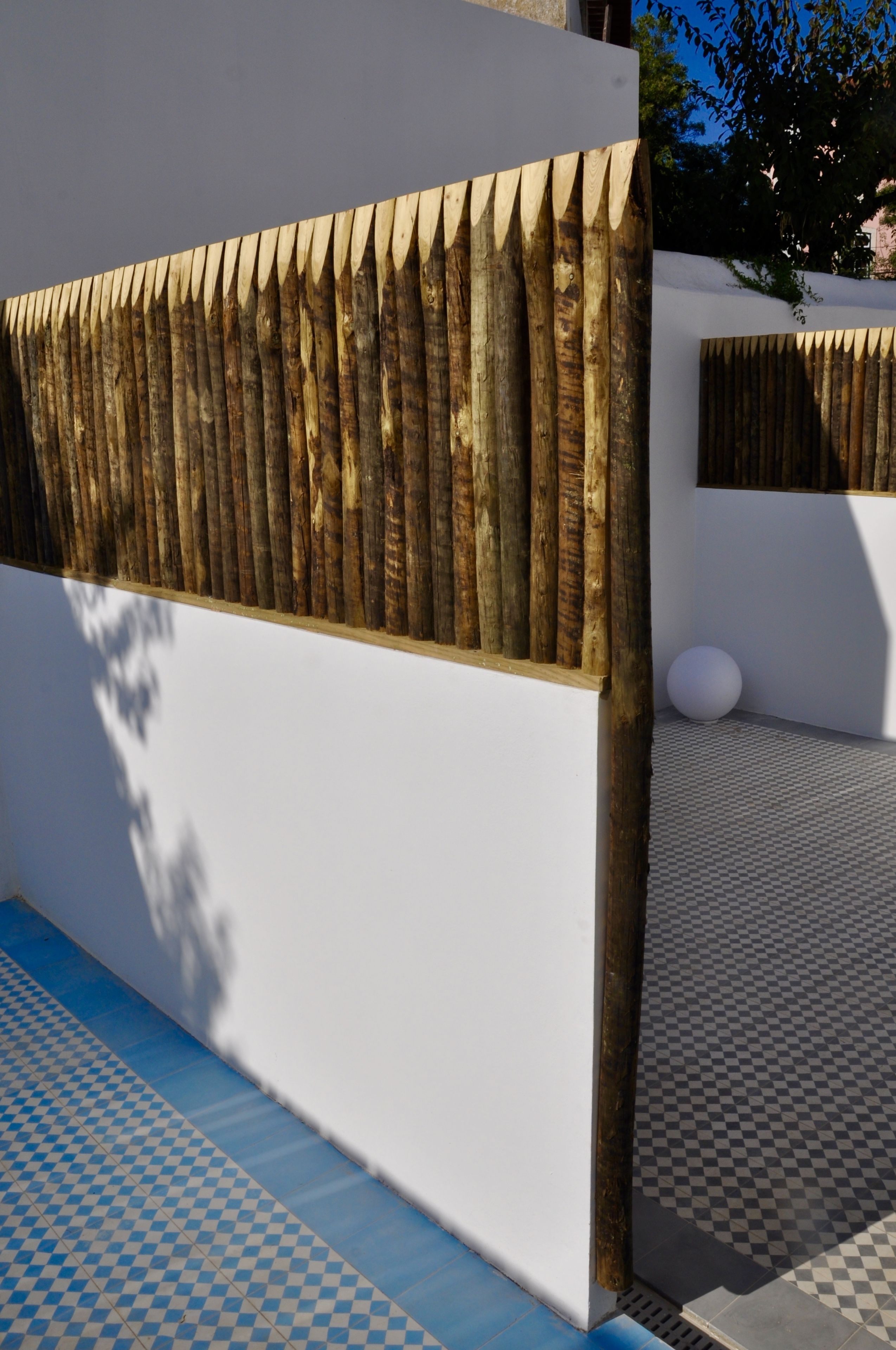 Un bâtiment moderne à l’extérieur blanc, doté d’un mur à lattes de bois, d’un sol à carreaux et d’un objet sphérique blanc posé sur un socle.