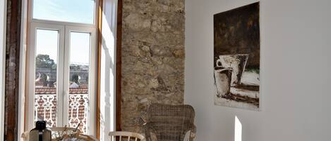 A dining area with a stone wall, a wicker chair, a table with a tray, and a painting on the wall.