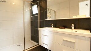 A modern bathroom with a glass shower enclosure, a white vanity with two sinks, and a large mirror above the vanity.