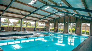 An indoor swimming pool with a wooden deck area, large windows, and a high ceiling with exposed beams. - EuroParcs Bad Hulckesteijn (Nijkerk)