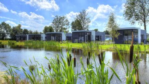 A modern building complex with a pond in the foreground, surrounded by greenery and trees. - EuroParcs Bad Hulckesteijn (Nijkerk)