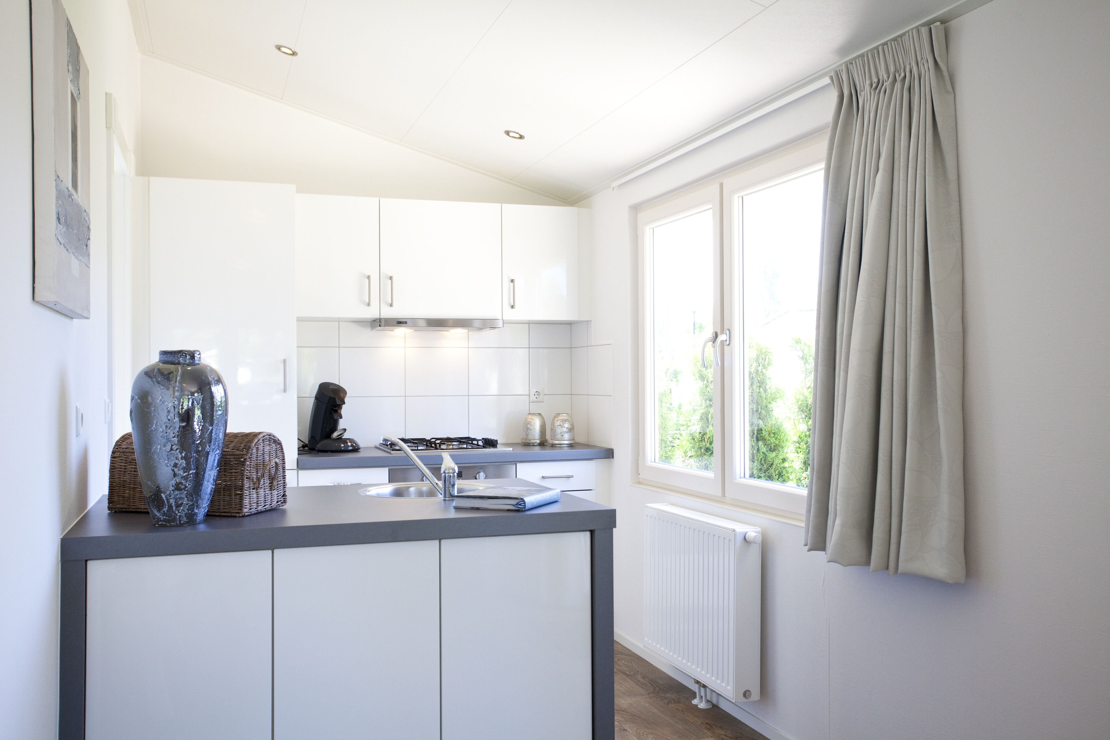 A modern kitchen with white cabinets, a built-in stove, and a window with curtains.