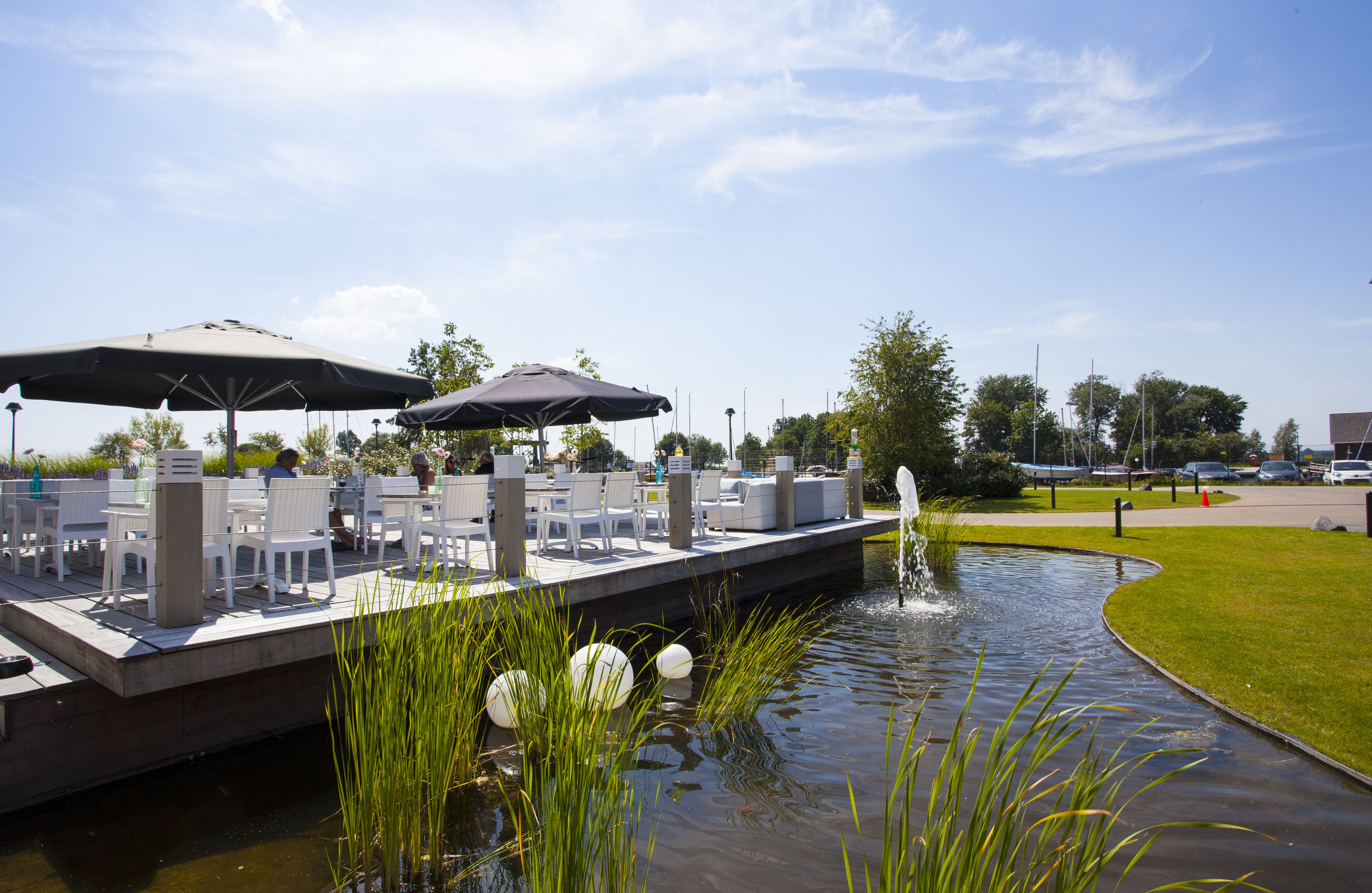 An outdoor patio with white chairs and tables, umbrellas, and a small water feature.