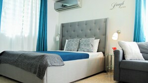 Une chambre à coucher moderne avec une tête de lit capitonnée grise, un lit recouvert d’une couvre-lit bleue et blanche, et un fauteuil gris.