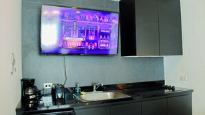 Une cuisine équipée d’un téléviseur à écran plat fixé au-dessus d’un plan de travail noir, d’une machine à café, d’un grille-pain et d’un évier.