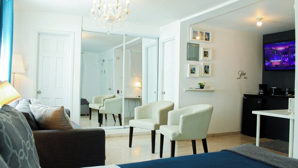 Une chambre d’hôtel comprenant un lit, un canapé, deux fauteuils, un bureau, une télévision, un miroir et un lustre.