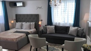 Ein modernes Hotelzimmer mit einem großen Bett, einer Couch, zwei Sesseln, einer Kristallleuchtre und einem Fernseher.