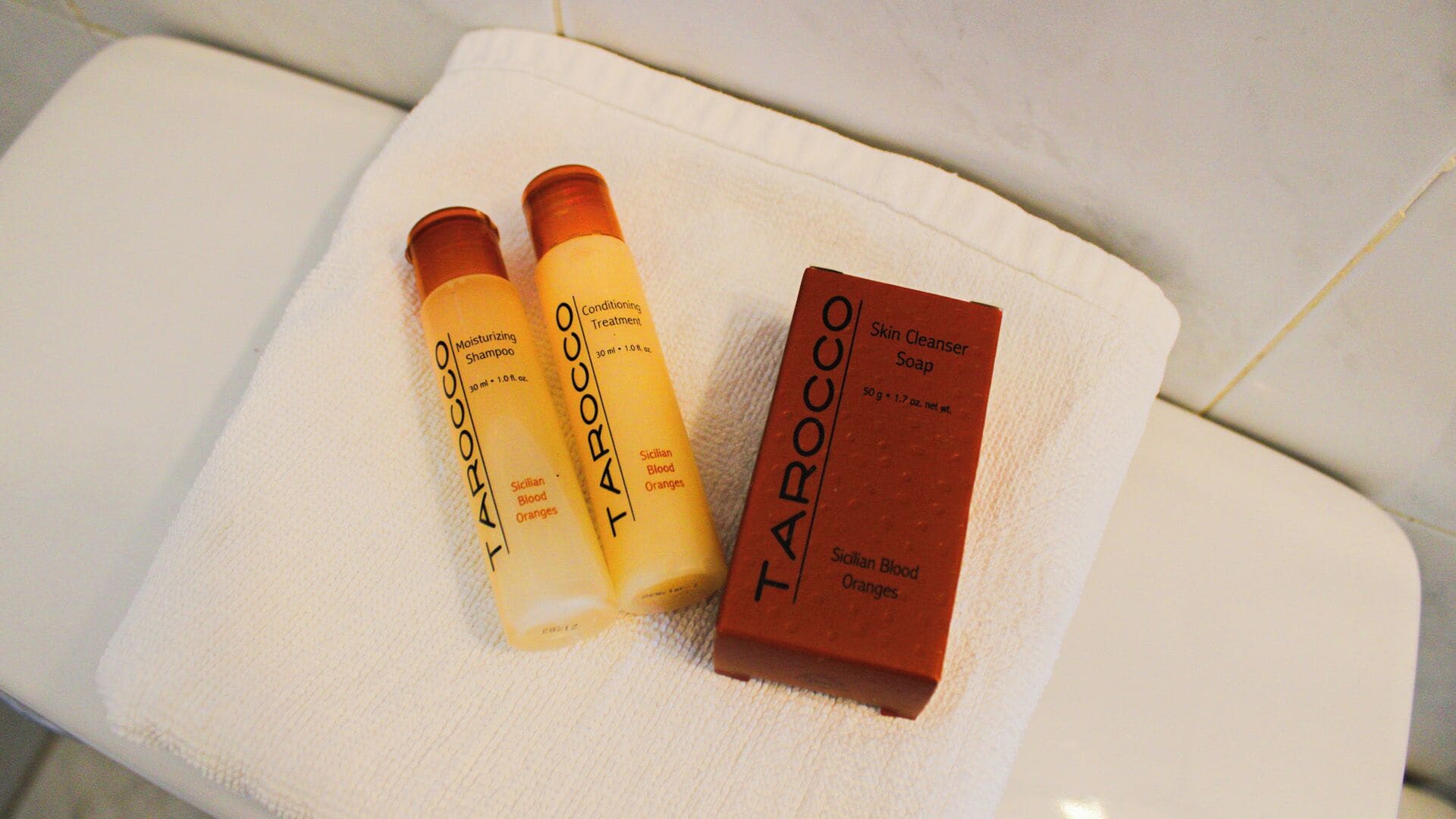 A white bathroom bench with two bottles of Tarocco Moisturizing Shampoo and a bar of Tarocco Skin Cleanser Soap.