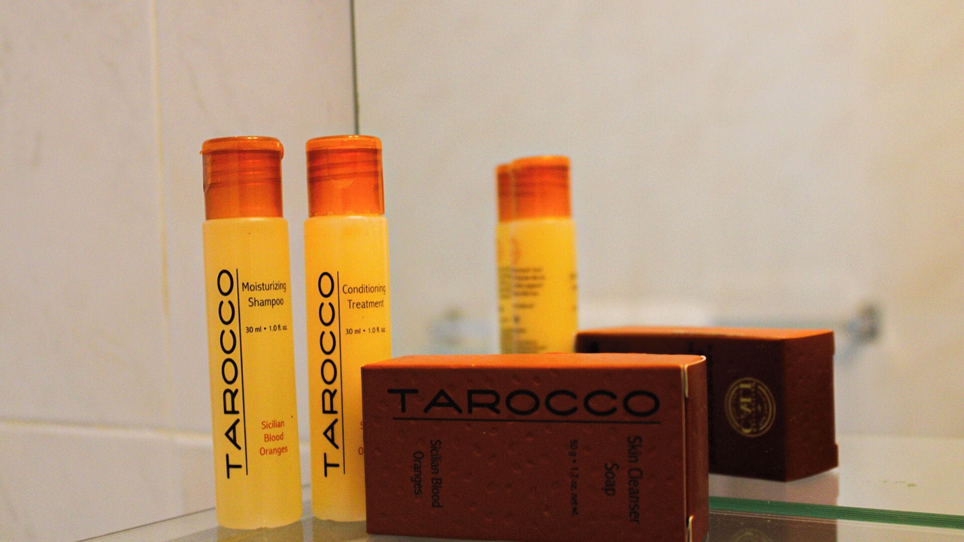 Three bottles of Tarocco skincare products and a box on a reflective surface.