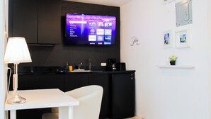 A modern kitchen with a flat-screen TV mounted above the counter, a white table, and a black refrigerator. - Chandelier 202 (Ponce)