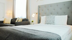 A hotel room with a large bed, a grey upholstered headboard, and a sofa with cushions.