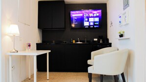 A modern kitchen with a flat-screen TV mounted above the counter, a white table with a lamp, and a white chair. - Chandelier 202 (Ponce)