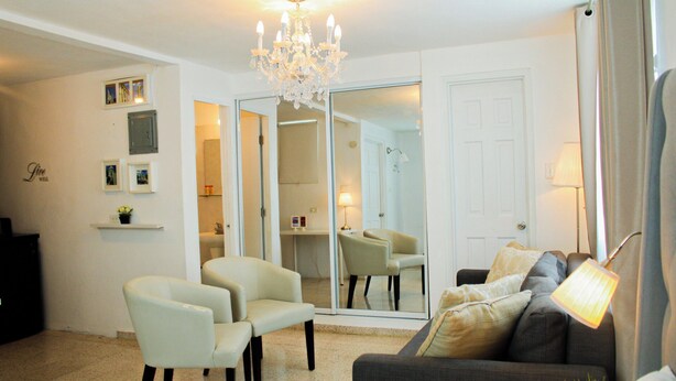 A living room with a chandelier, a sofa, two armchairs, a dining table with chairs, and a sliding glass door leading to a bathroom. - Chandelier 202 (Ponce)