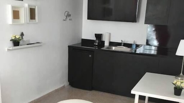 A modern living room with a white armchair, a small table, and a flat-screen TV mounted on the wall. - Chandelier 302 (Ponce)