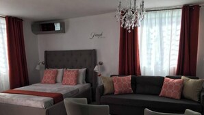 A modern bedroom with a bed, sofa, two armchairs, a chandelier, and a wall-mounted TV. - Chandelier 302 (Ponce)