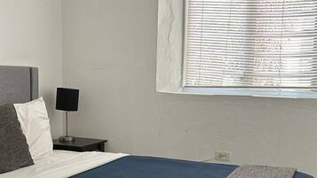 A bedroom with a bed, a nightstand, a lamp, and a window with blinds.