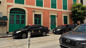 Un edificio con contraventanas verdes y fachada roja, que cuenta con un estacionamiento y varios coches.