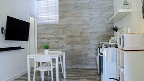 A compact kitchen with a flat-screen TV, a small dining table with chairs, a potted plant, and a microwave.