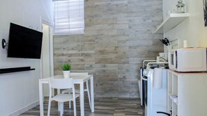 Compact kitchenette with a flat-screen TV, dining table, and potted plant, equipped with a microwave, coffee machine, and refrigerator.