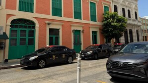 A building with green shutters and a white facade, parked cars, and a clear blue sky. - Gladiolas 1104 (Ponce)