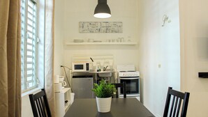 A dining area with a table, chairs, a potted plant, a microwave, a sink, and a stove in the background. - Gladiolas 1104 (Ponce)