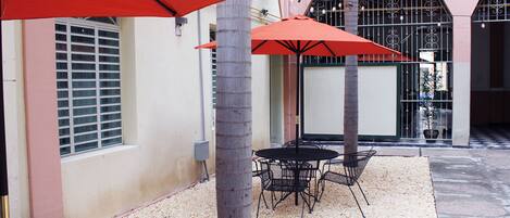 Un patio con mesa y sillas, sombrillas rojas y una palmera.