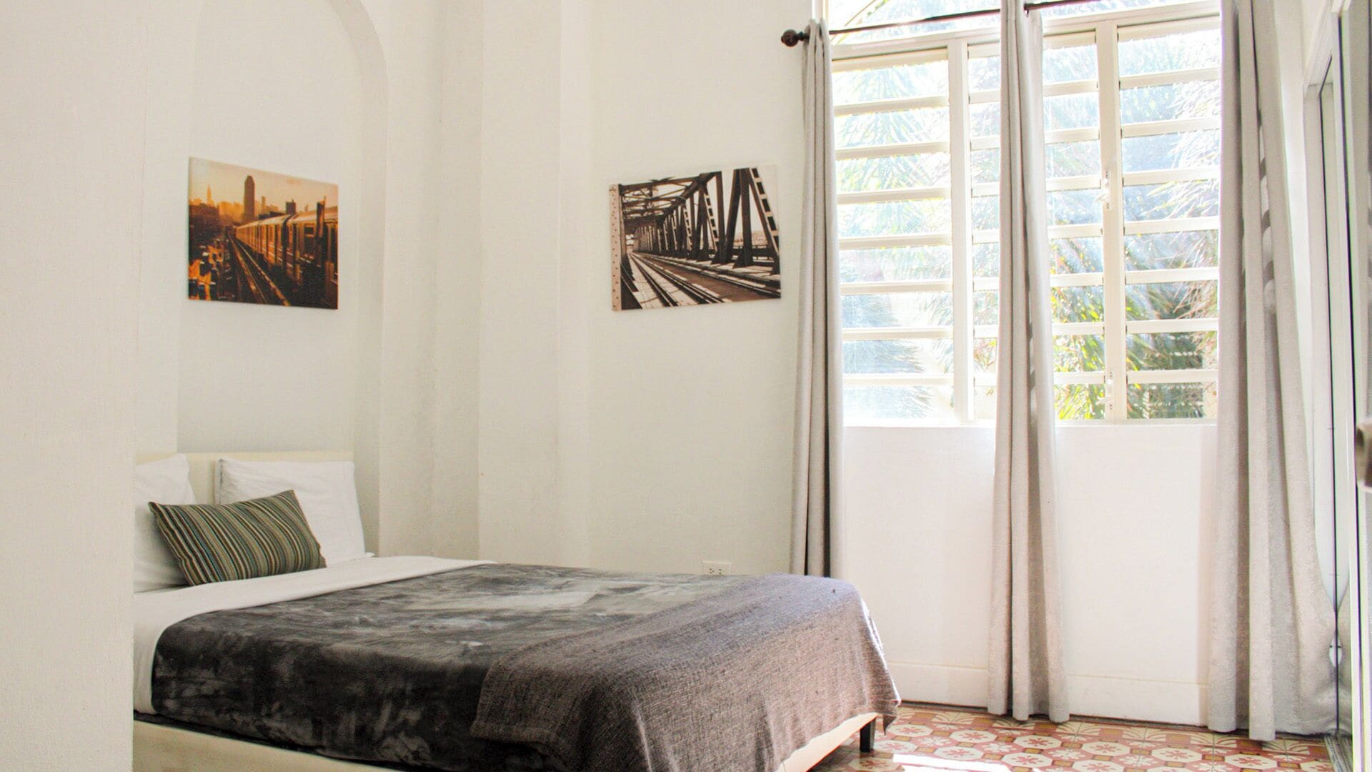 A bedroom with a bed, a window with curtains, and two wall-mounted pictures.