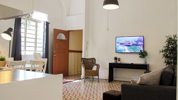 A living room with a television, a dining area with chairs, a wicker chair, a sofa, and a plant. - Gladiolas 1205 (Ponce)