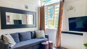 Un salon moderne avec un canapé gris, des coussins à motifs, un grand miroir, un téléviseur à écran plat et une fenêtre avec des rideaux.